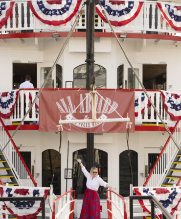 A woman stands on a boat decorated with fourth of july banners