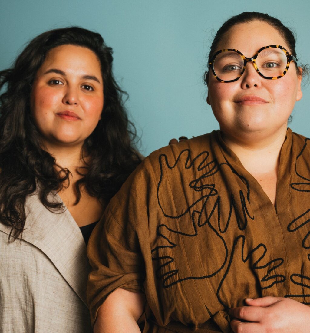 A portrait of two women against a teal background
