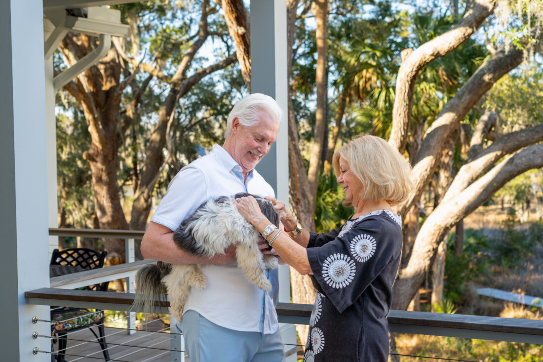 A couple pets a dog on a porch
