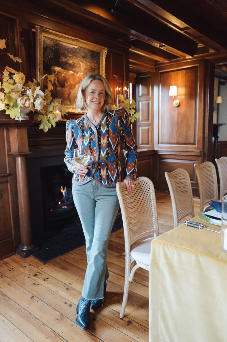 A woman in a patterned blouse stands in a wood-paneled dining room