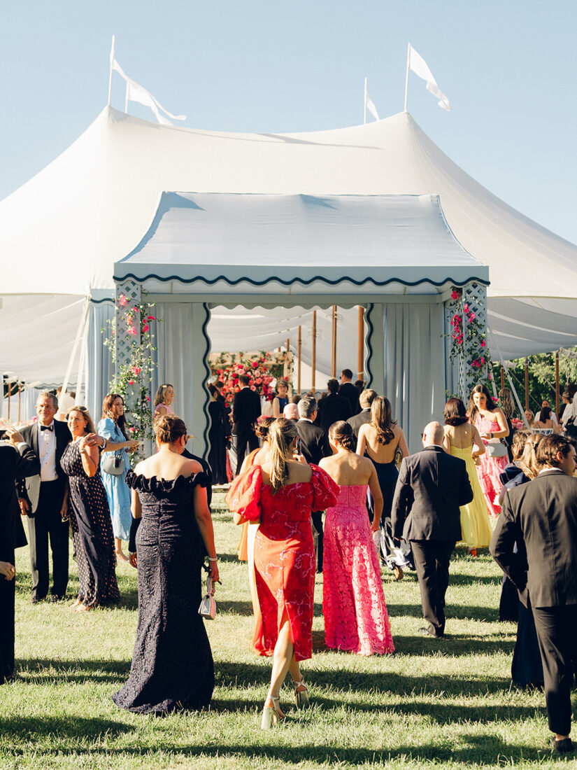 Wedding party guests walk into a tent with a sage trellis