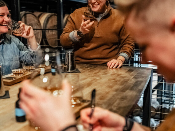 People at a table laugh and drink bourbon and take notes