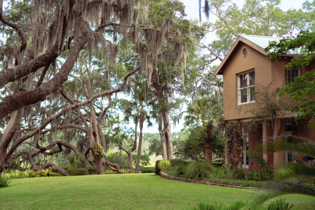 A brown pueblo style home with tall oak trees