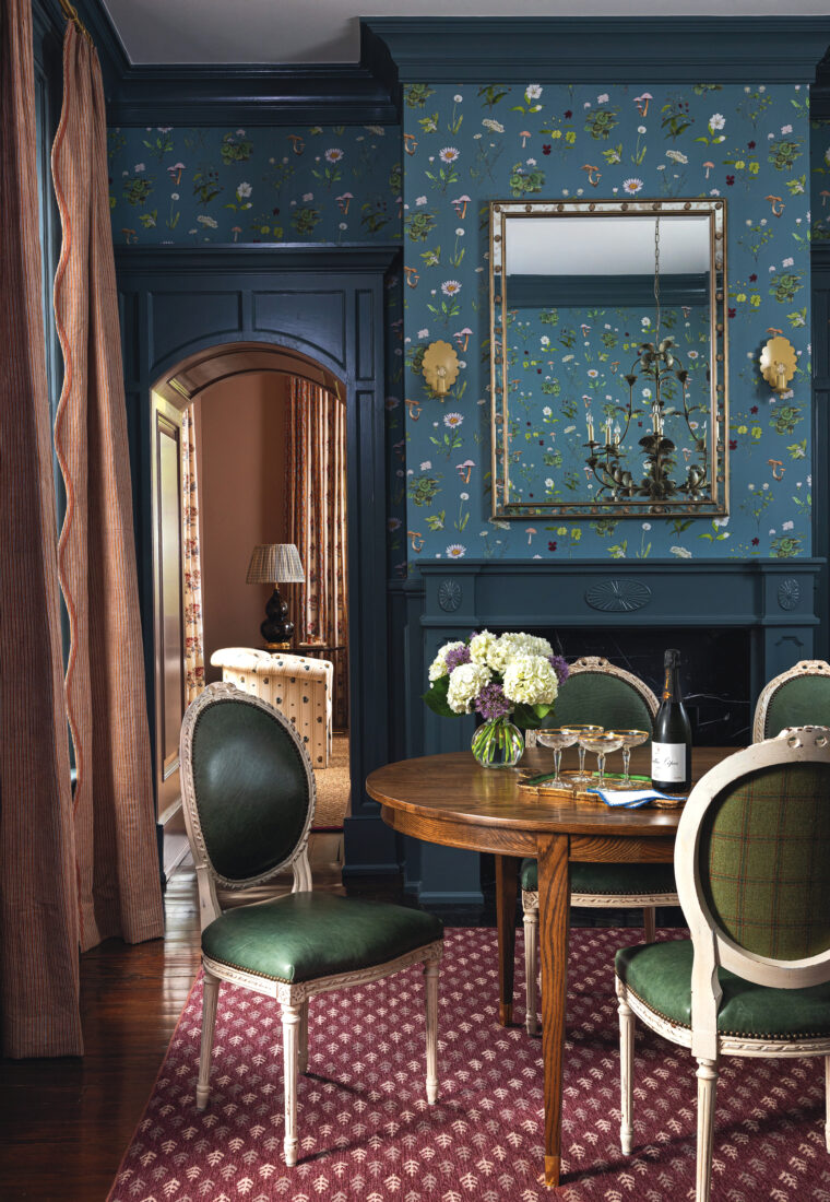 A dining room with navy trim and navy floral wallpaper and a red patterned rug