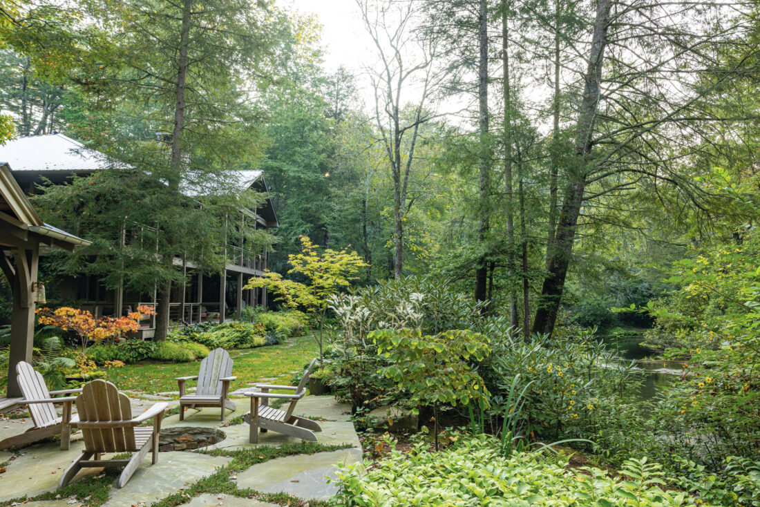 A garden at the back of a house in woodland. It has a firepit surrounded by chairs