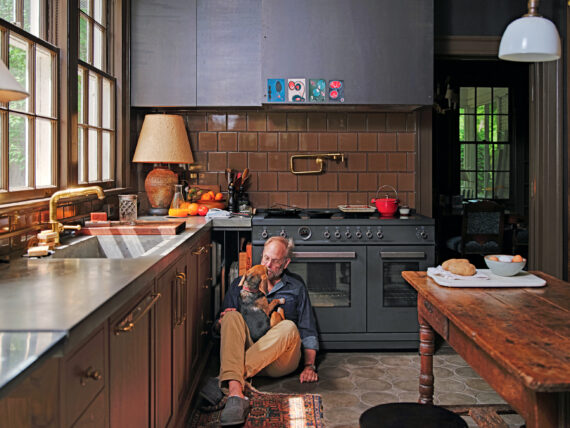 A man sits on a kitchen floor with a beagle in his lap