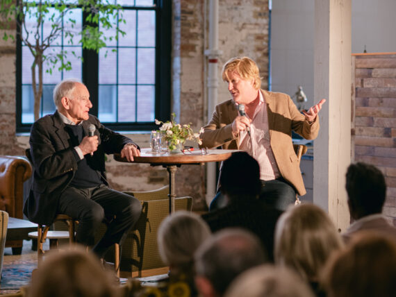 Two men sit at a table during an interview in a rustic office.