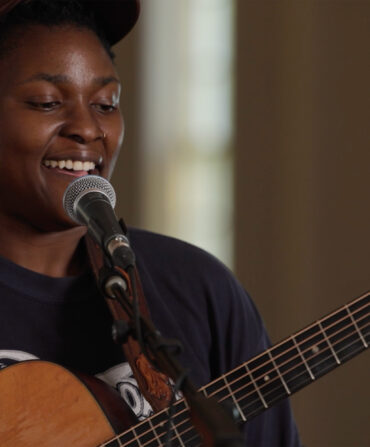 A woman holding a guitar at a microphone
