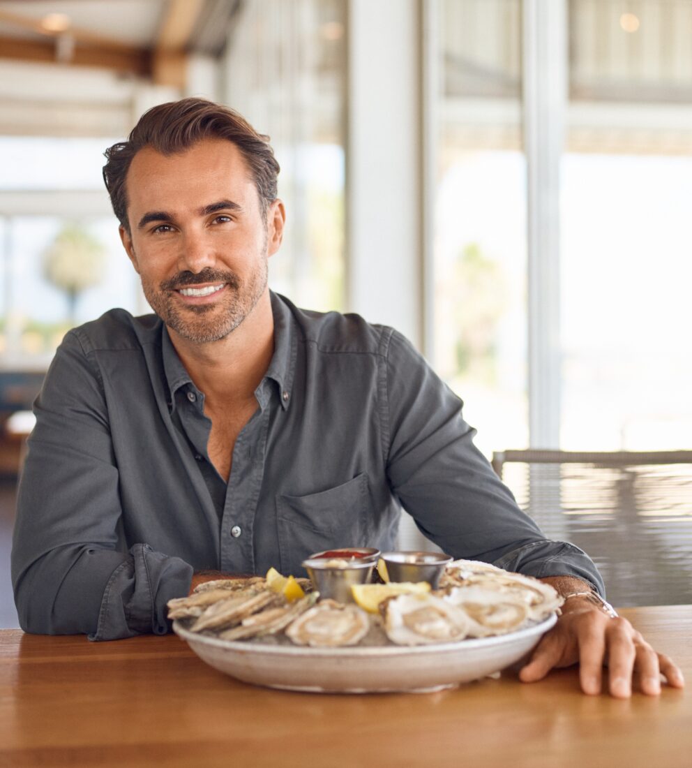 A man sits at a table with a tray of oysters