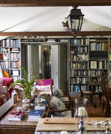 A layered, maximalist living room with stacks of books and colorful pillows