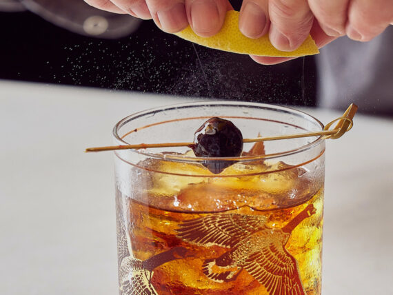 A hand twists a lemon peel over an old-fashioned