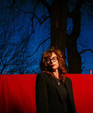 A woman with glasses stands outside in front of a red drop cloth